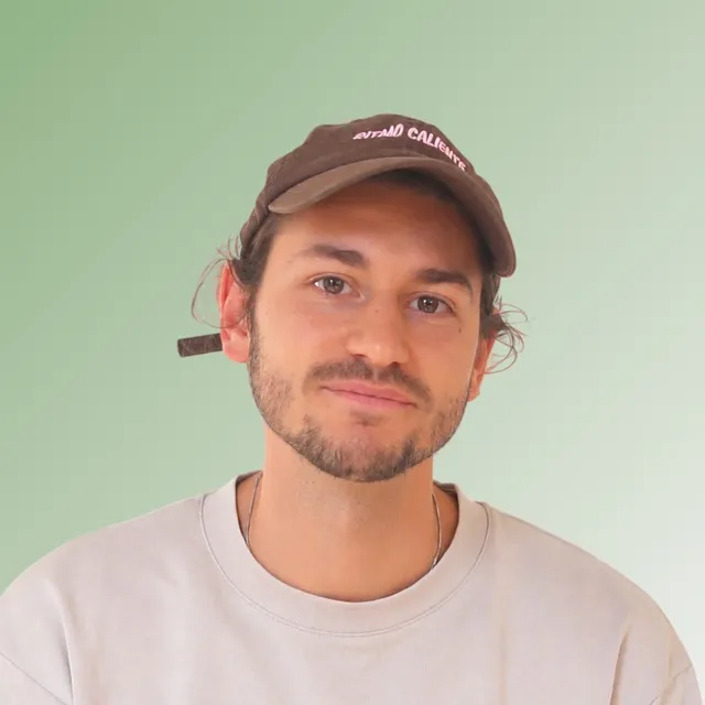 Portrait of Rayane Zidane in a brown cap and a light grey sweater against a soft green background.